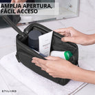 Neceser de cuero negro con amplia apertura, manos sostienen la cremallera, productos de aseo en el interior, toalla y espejo, STILORD visible